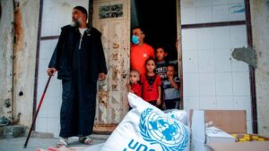 Members of a Palestinian family, some clad in masks due to the coronavirus pandemic, stand through the door of their home as they receive food aid provided by the United Nations Relief and Works Agency for Palestine Refugees (UNRWA) in Gaza on September 15, 2020.